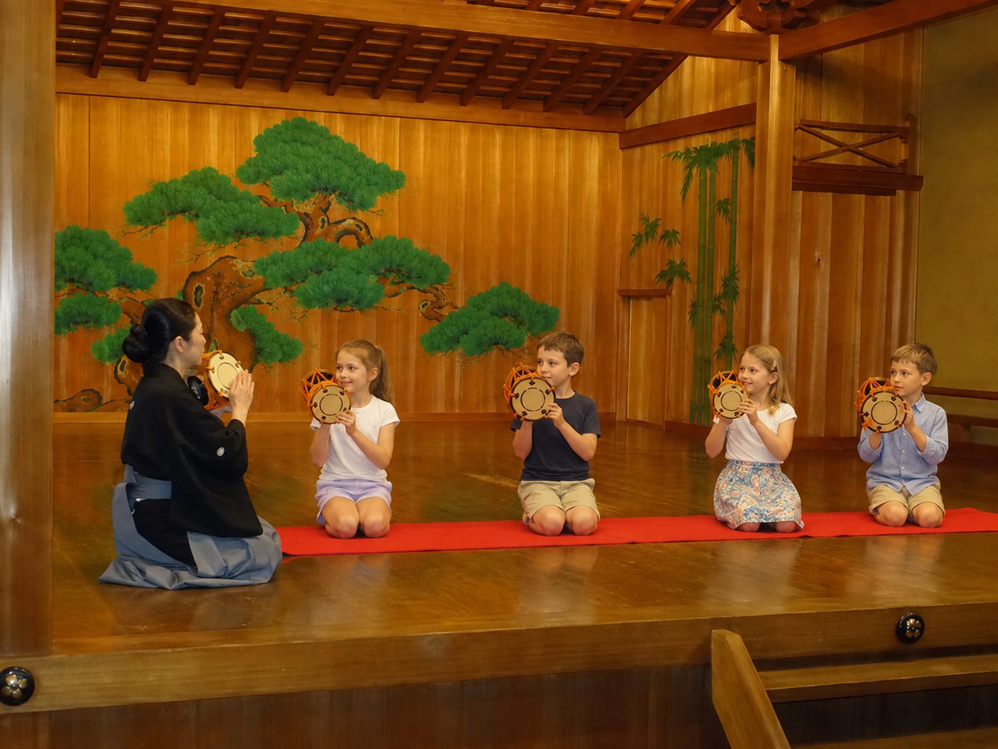 Illustration of children trying the Noh hand drum on stage with a performer