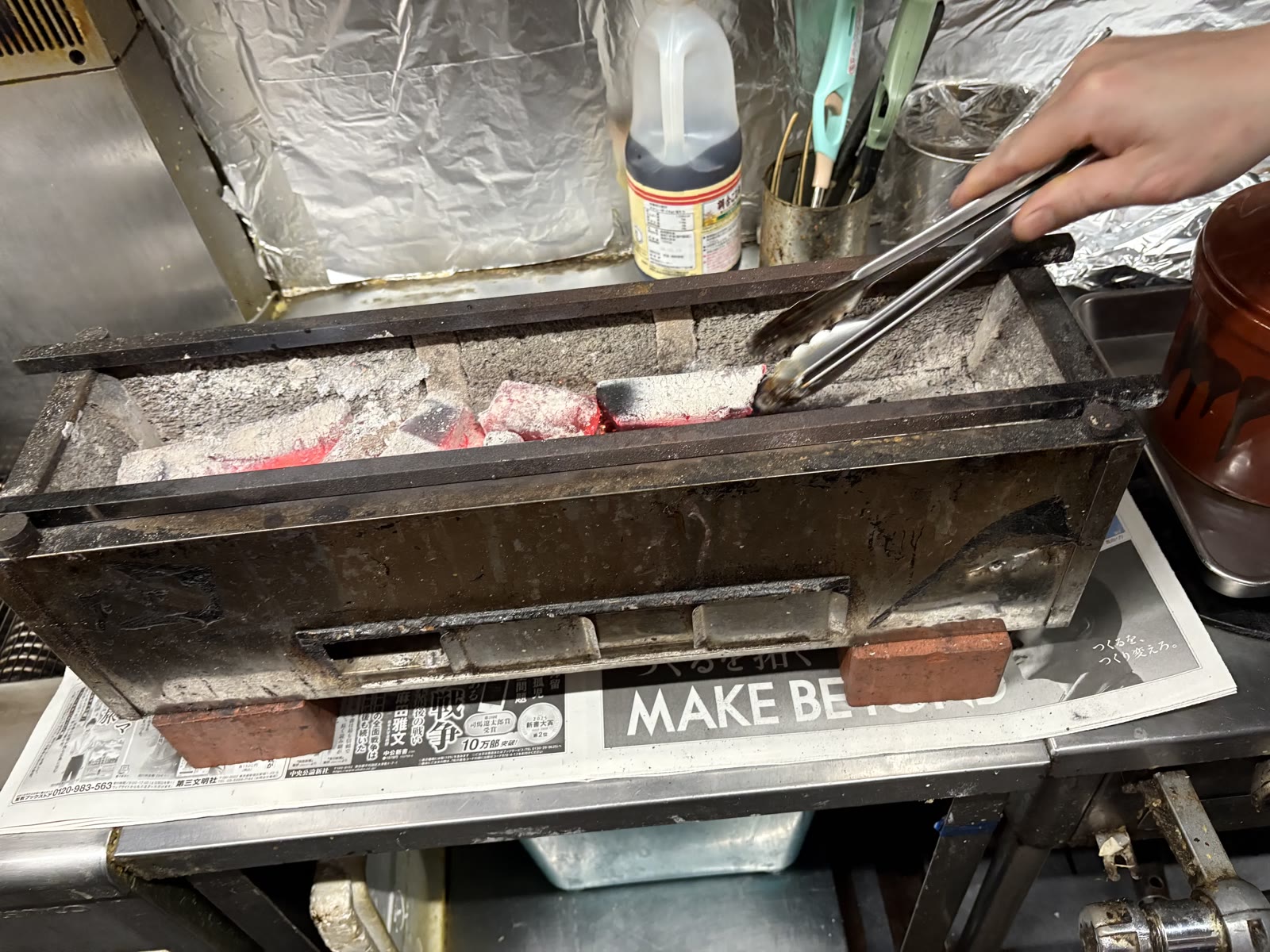 Glowing charcoal being arranged in the grill with tongs
