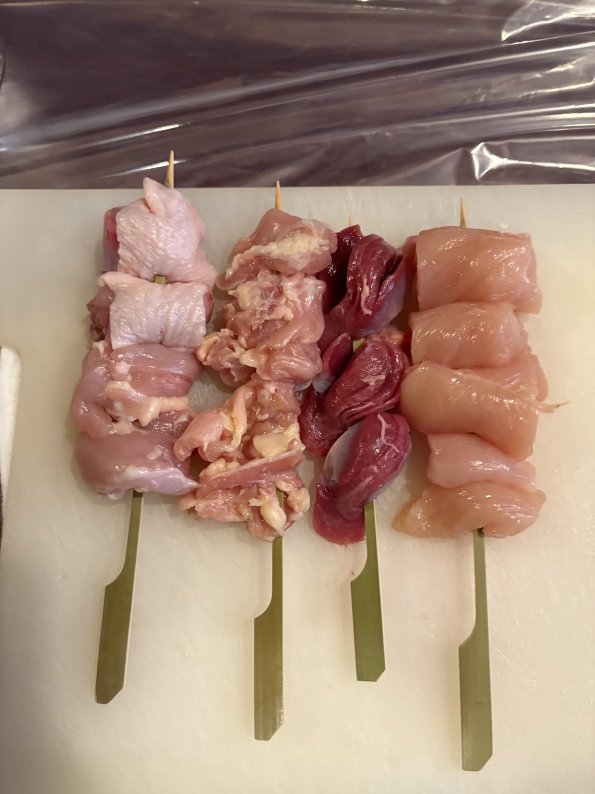 Four freshly skewered sticks of chicken lined up on a cutting board